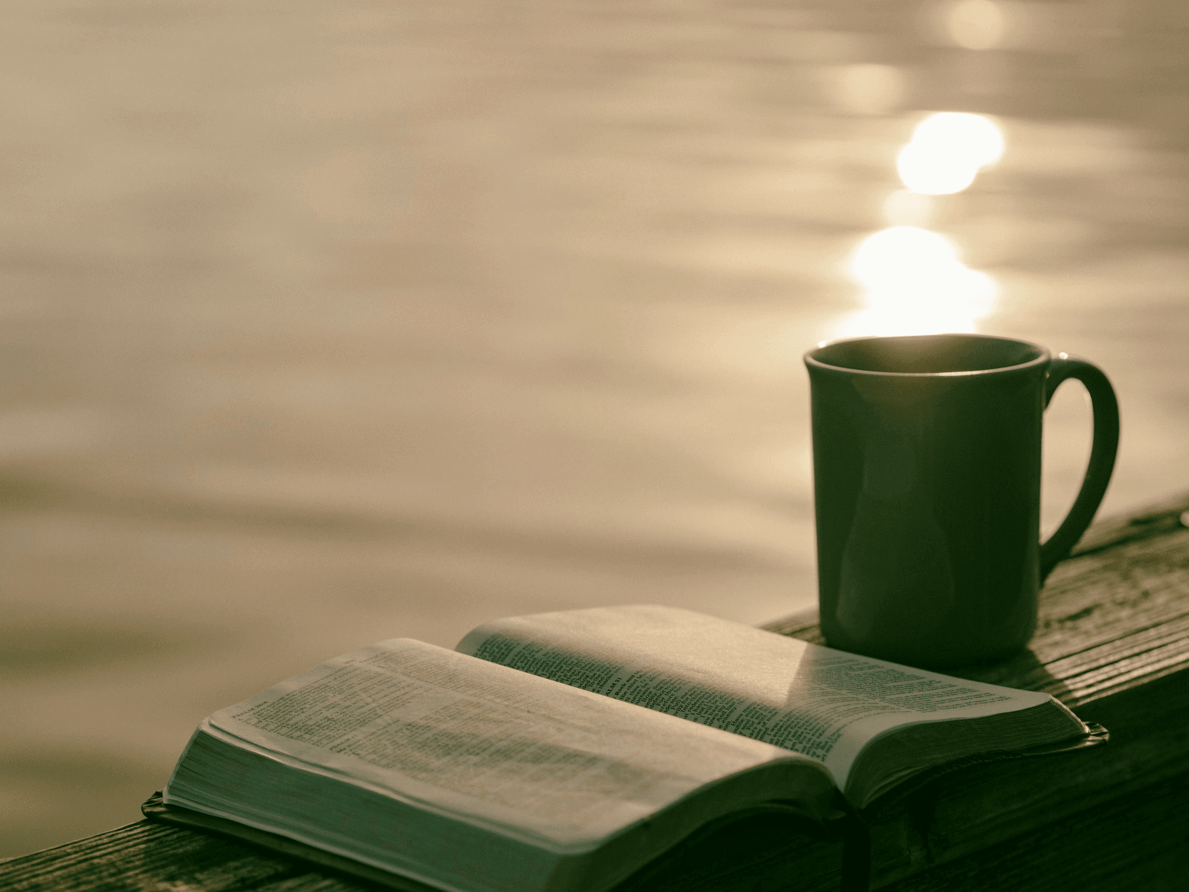 Green ceramic mug beside the Bible by water